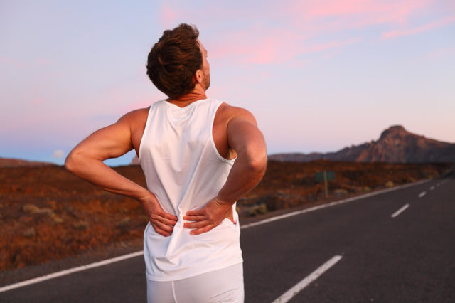 man holding his back, standing on the road